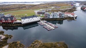 An aerial view of a coastal area with a marina, several buildings, and boats docked. - Sula Rorbuer og Havhotell (Frøya)