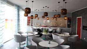 A modern interior with multiple round tables and chairs, hanging wicker pendant lights, and a view of sailboats through large windows. - Sula Rorbuer og Havhotell (Frøya)