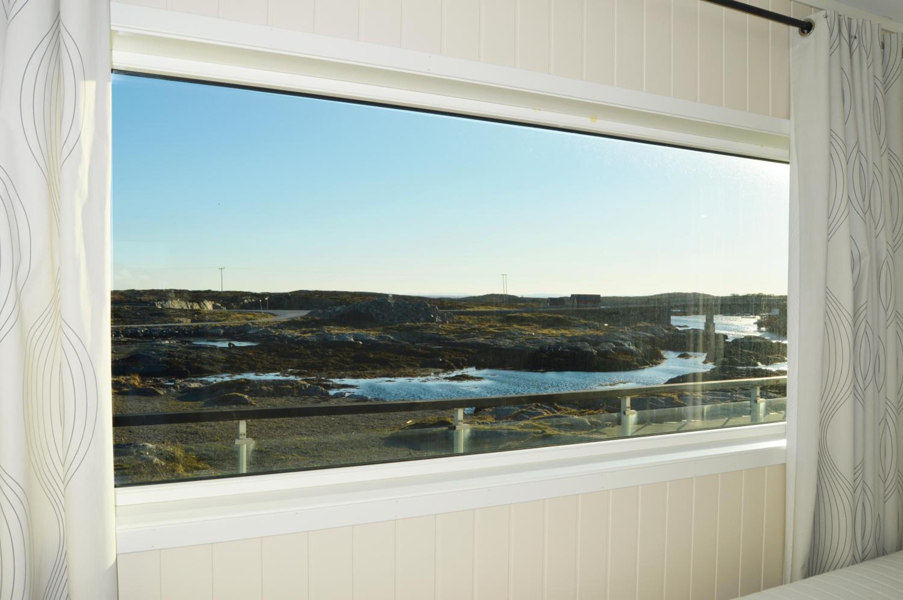 Ett rum med ett stort fönster som ger utsikt över en klippig kustlinje och ett vattenområde.
