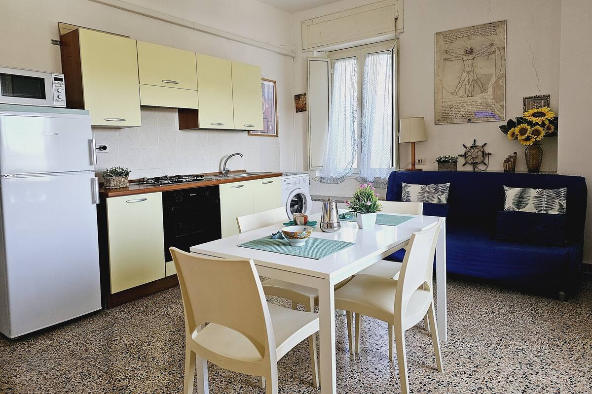 Une cuisine compacte avec un coin repas, un lave-linge et un canapé bleu agrémenté de coussins décoratifs.