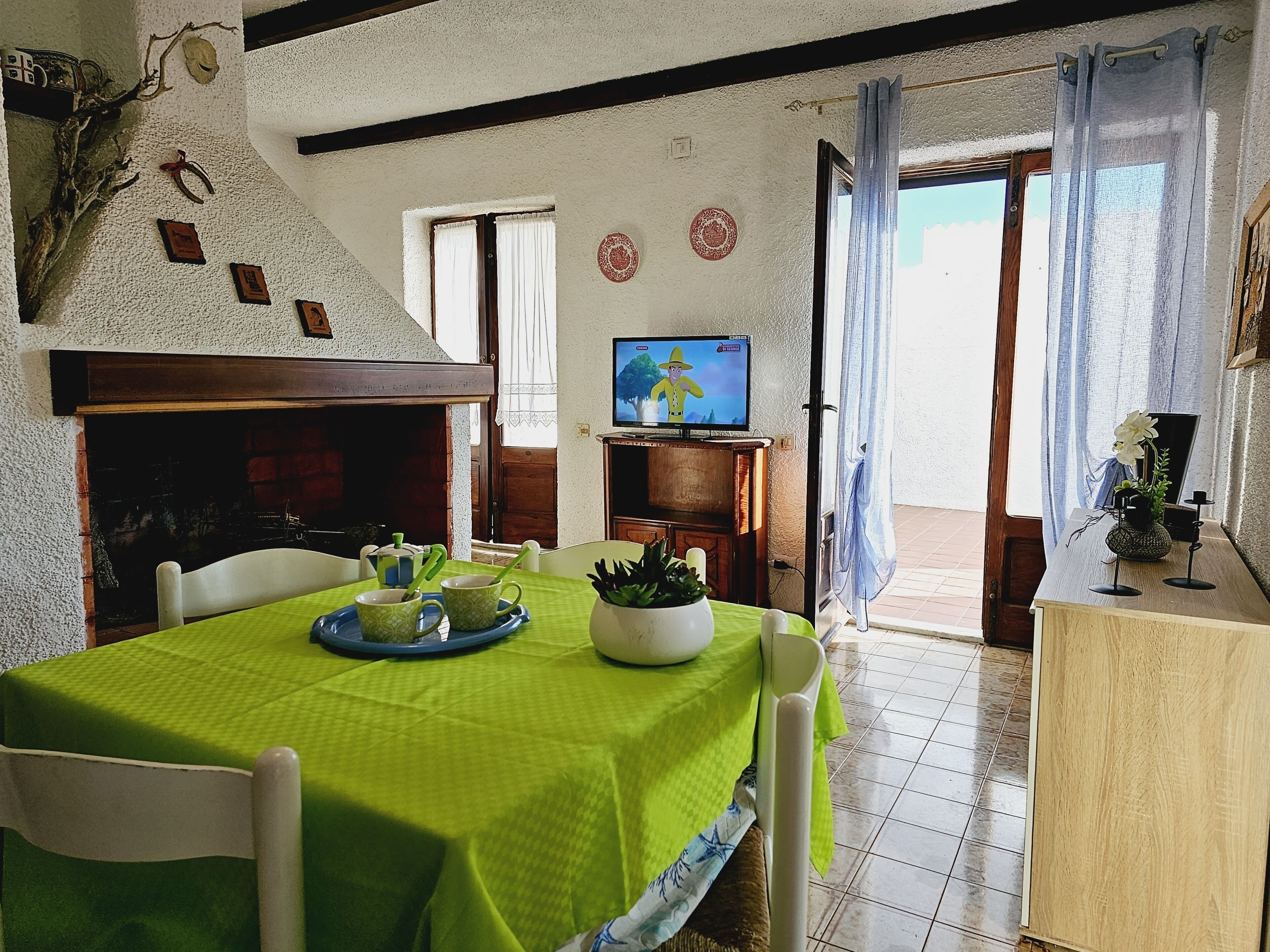 Een eethoek met een groene tafelkleed, stoelen, een televisie en een open haard.