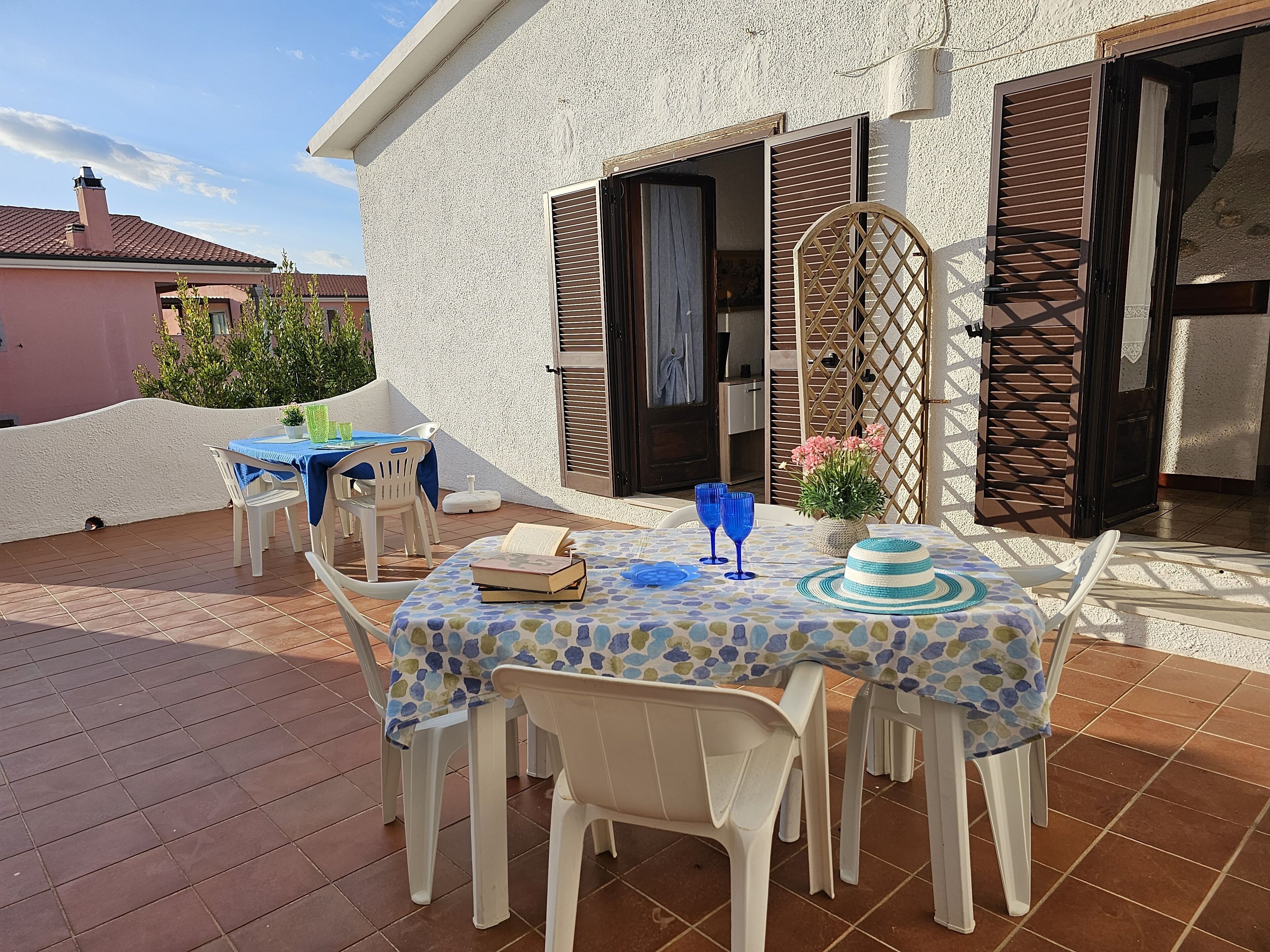 A patio with a table set for two, a chair, and a potted plant.