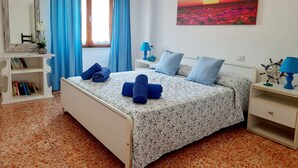 Een slaapkamer met een bed, nachtkastje, dressoir, raam met gordijnen, schilderij en een boekenkast.