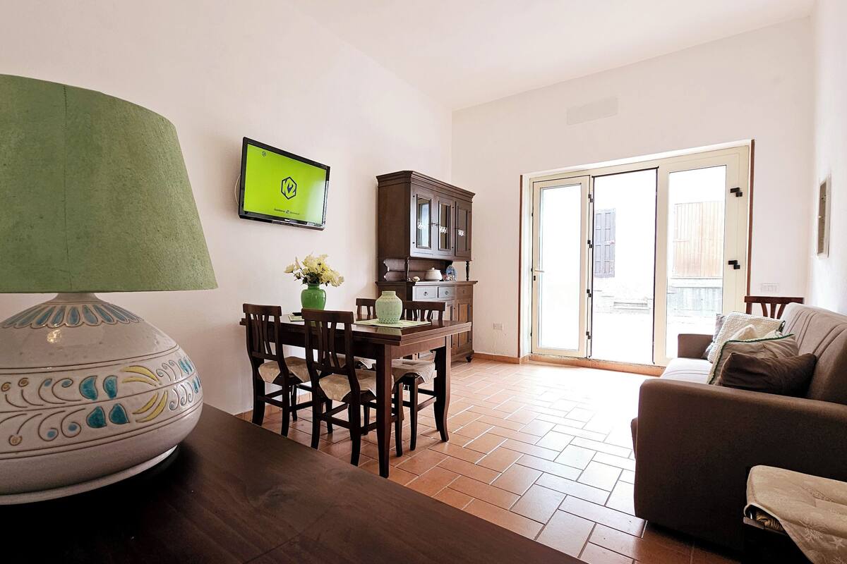 Un salon comprenant un coin repas, une lampe verte, un téléviseur et une vue à travers la porte vitrée.