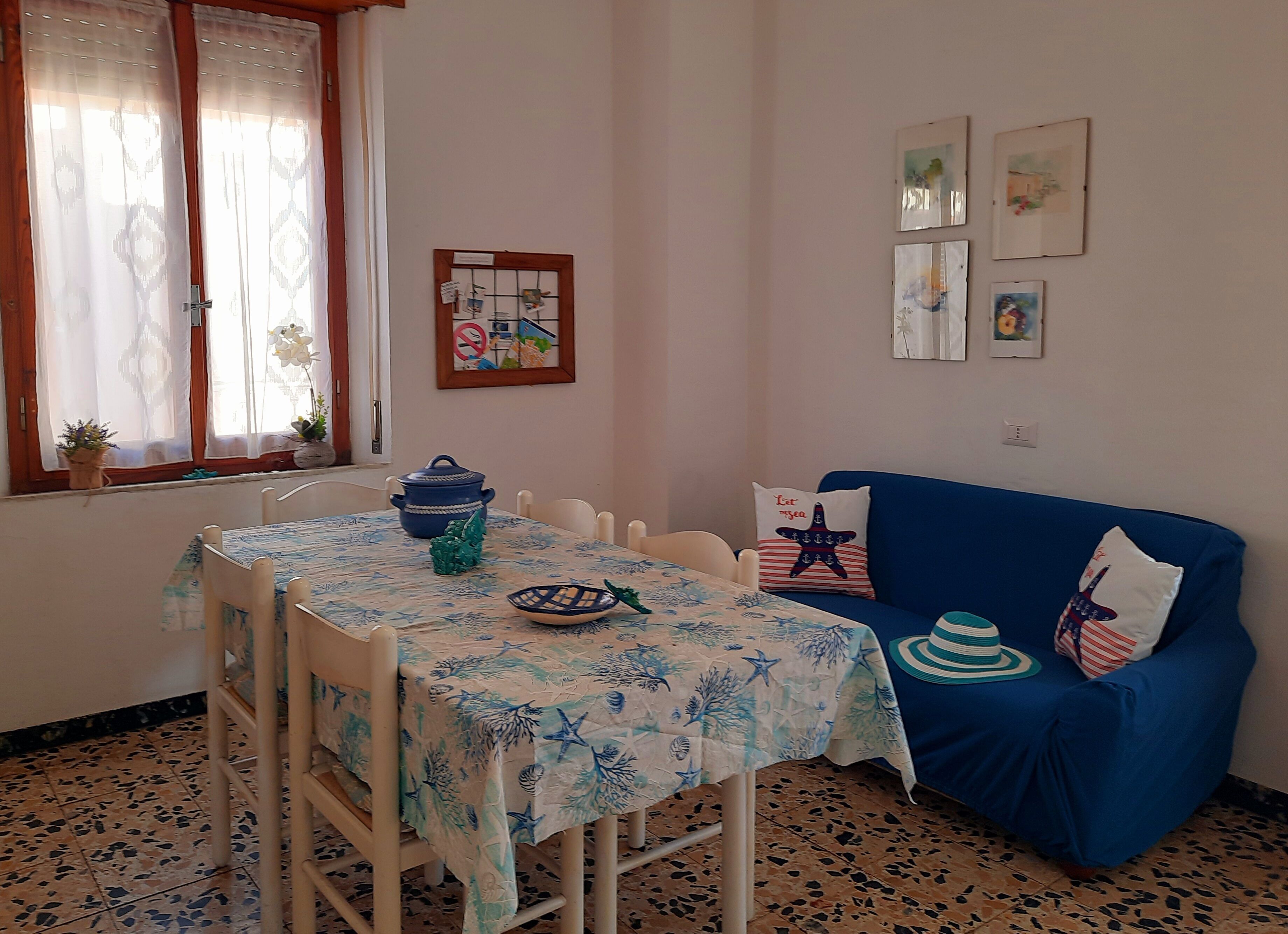 A dining area with a table set for two, a blue sofa, and a wall with framed artwork.