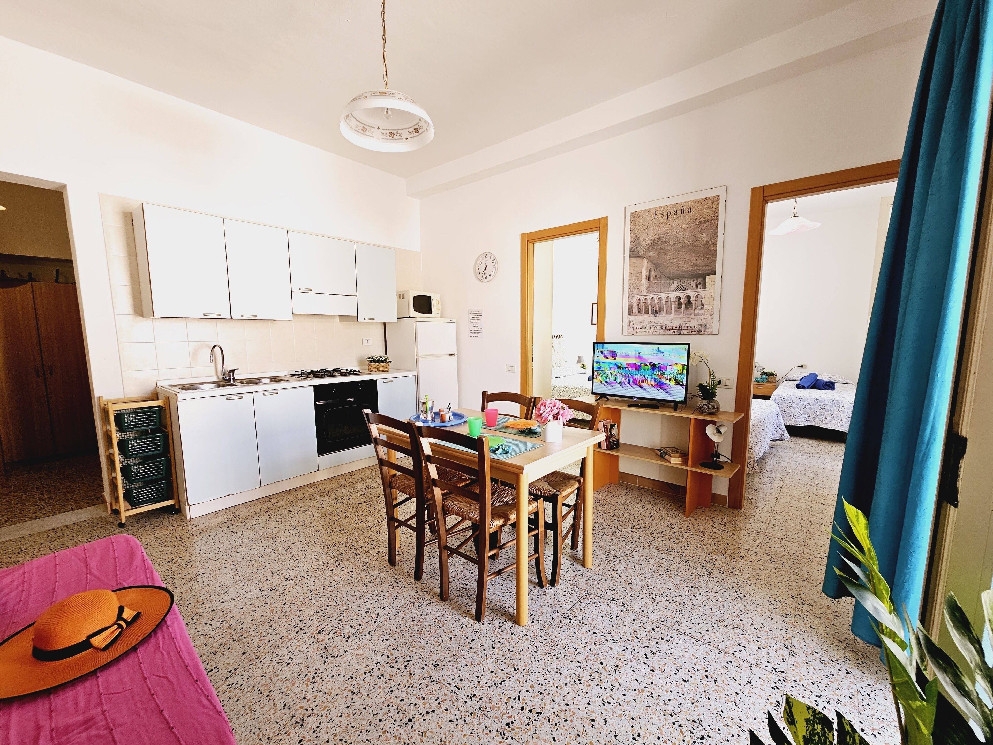 A compact kitchen with white cabinets, a microwave, and a gas stove. There is a dining area with a table and chairs, and a television on a stand.