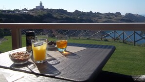 Een tafel met een kom ontbijtgranen, een blik citroenlimonade en twee glazen drank, met uitzicht op een kustlandschap met een vuurtoren.