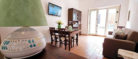 A living room with a wooden table, chairs, a sofa, a lamp, and a TV displaying 'Sonic the Hedgehog'.