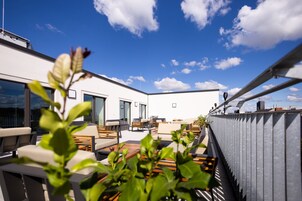 Una terraza en la azotea con mobiliario exterior, vistas al horizonte de la ciudad y un cielo azul despejado.