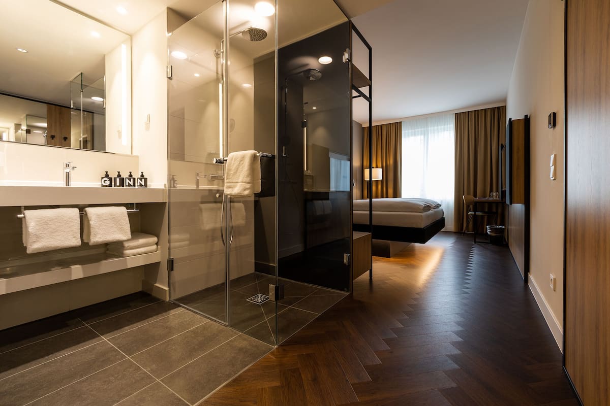 A modern hotel bathroom with a glass-enclosed shower, a large mirror, and a vanity with a sink and towel rack.