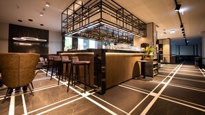 Zona de bar moderna con barra alta, varios taburetes y una amplia variedad de botellas y vasos.