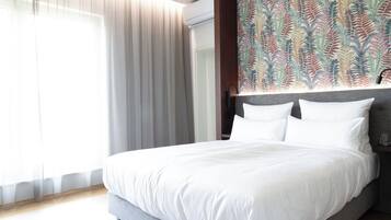 Una habitación de hotel moderna con una cama grande, un cabecero con papel tapiz estampado y un amplio ventanal con cortinas de gasa.