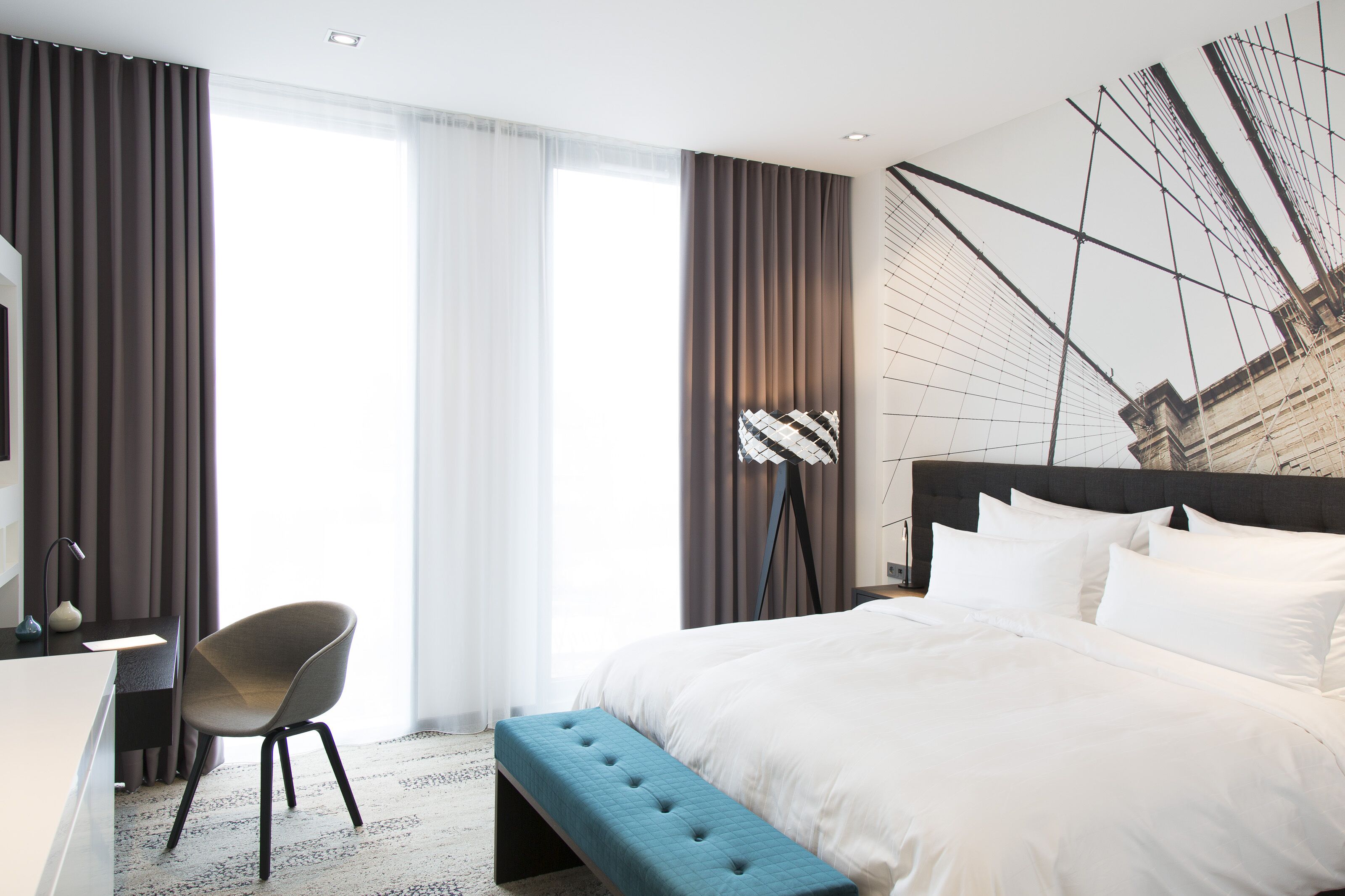 A modern hotel room with a large bed, a desk, and a chair.