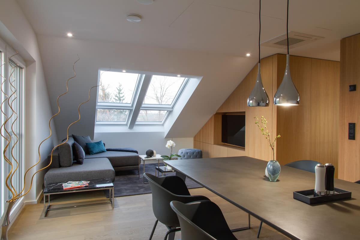 A modern loft-style room with a large skylight, a dining area with a long table, and a cozy seating area with a sofa and chairs.