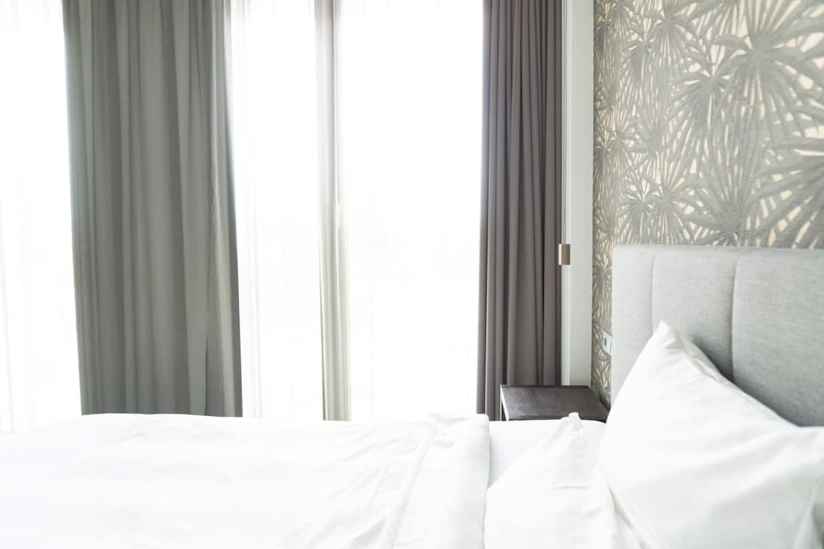 A neatly made bed with white linens, a grey headboard, and a patterned wall behind it.
