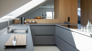 Une cuisine moderne avec un évier encastré, un couteau posé sur une planche à découper en bois et un saladier de fruits sur le plan de travail.