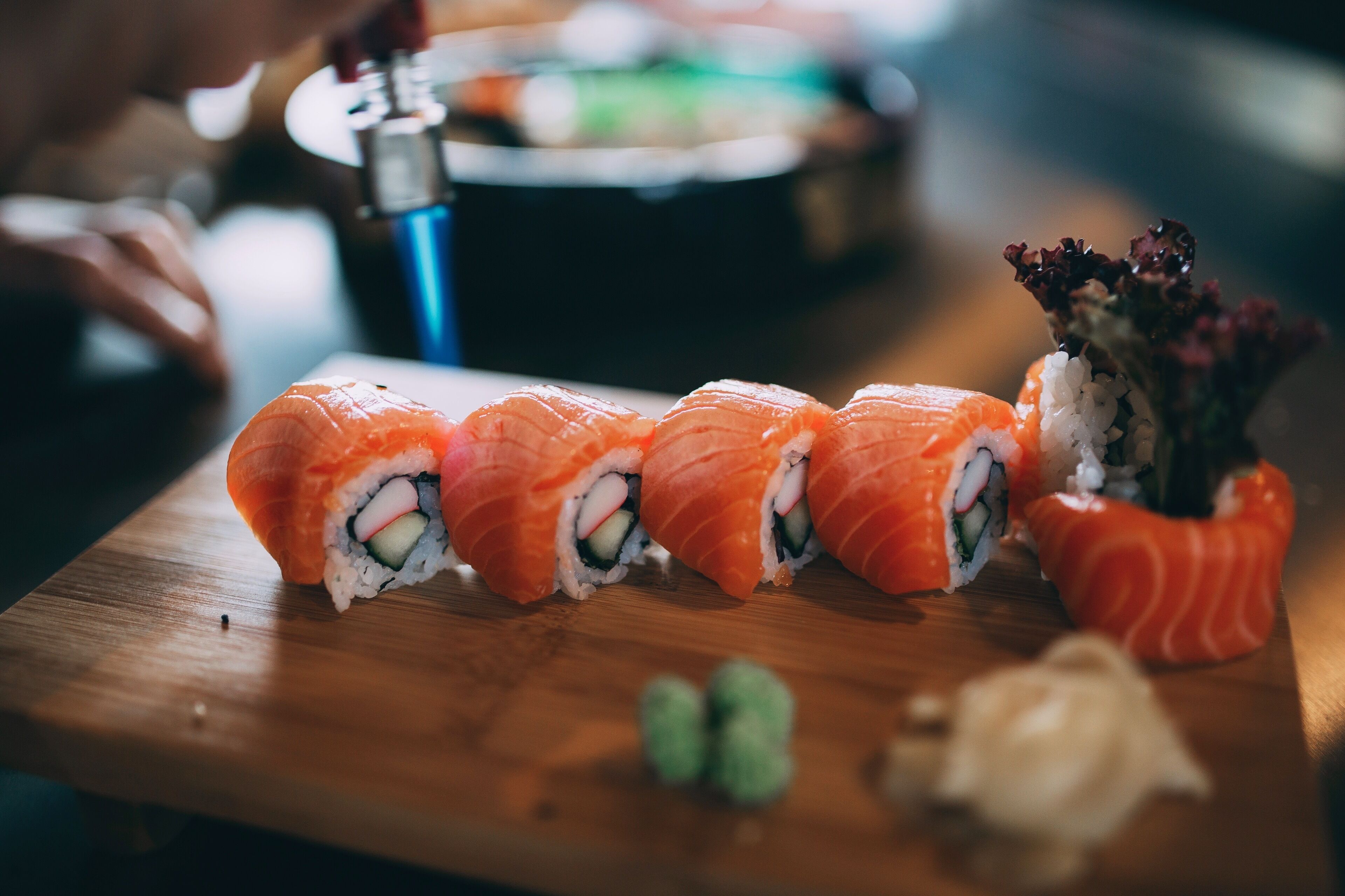 Une table en bois avec des sushis et un petit vase de fleurs.