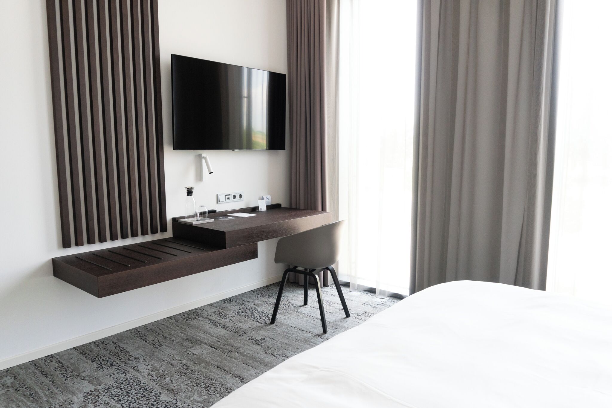 Habitació d'hotel moderna amb un llit, una taula de treball amb televisió de pantalla plana, un rentaplat i una cadira.