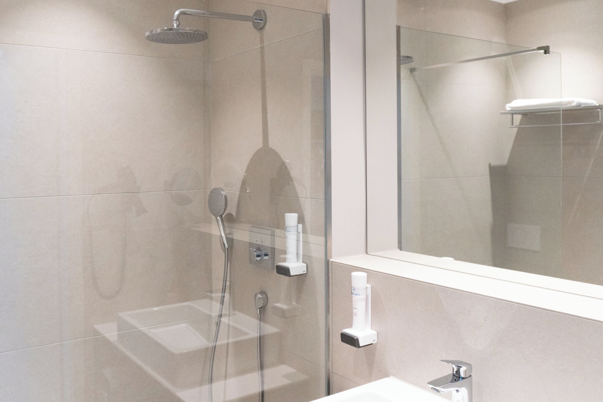 Un baño moderno con ducha envuelta en vidrio, un lavabo blanco y un espejo sobre él.