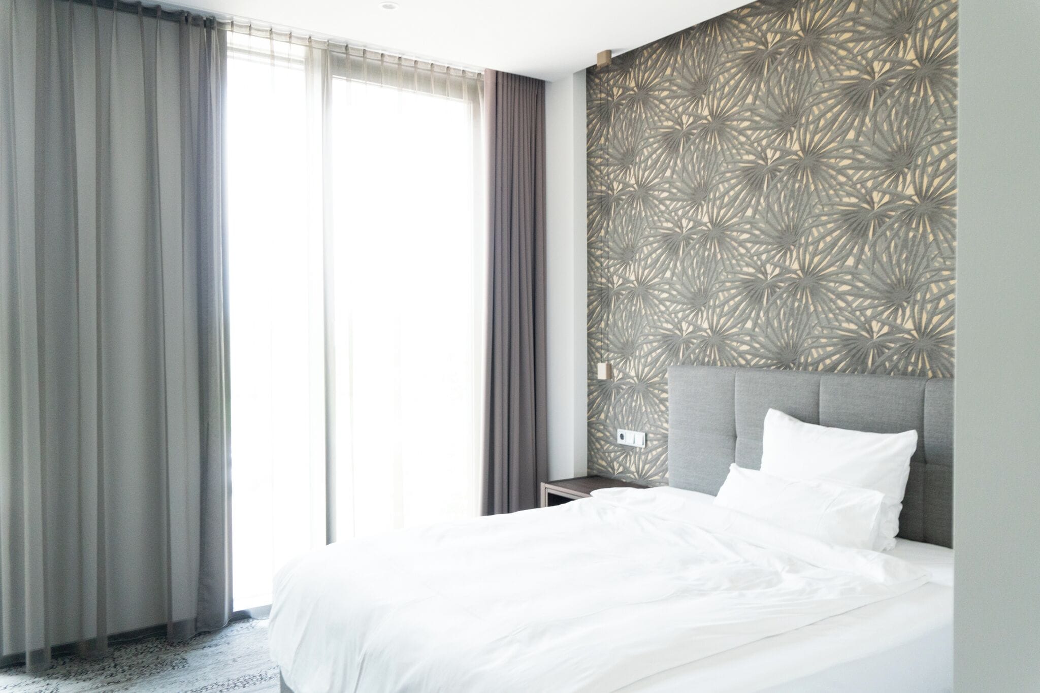 A hotel room with a large bed, a nightstand, and a patterned wall.
