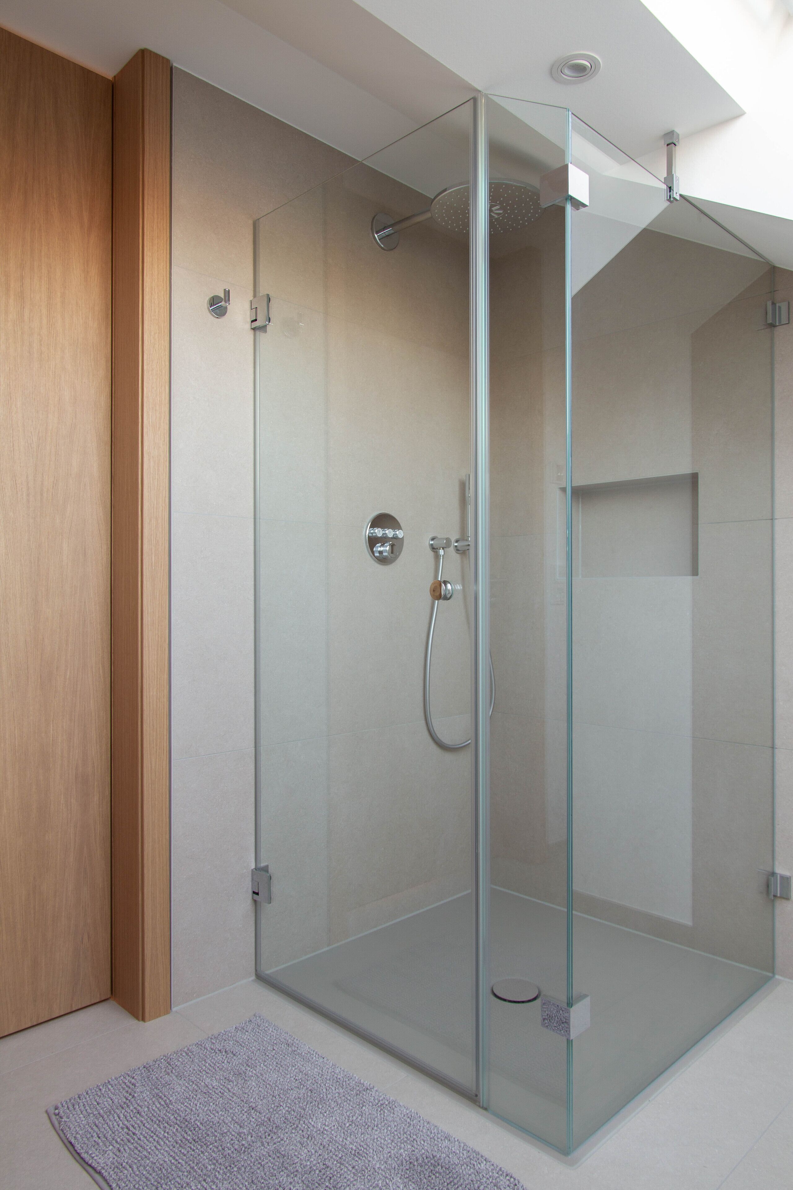 A modern bathroom with a glass-enclosed shower, a wooden door, and a light-colored floor.