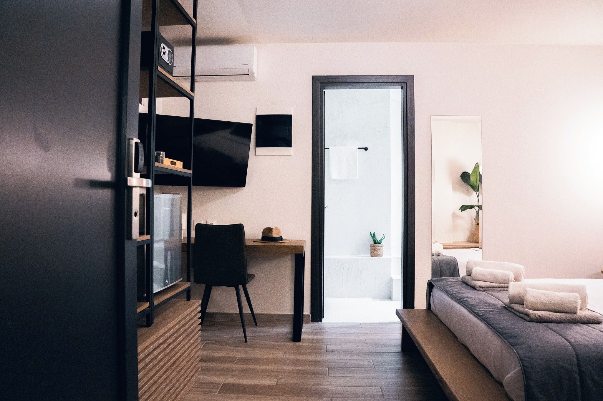 Quarto de hotel moderno com cama, escrivaninha, cadeira, televisão e porta que dá para uma varanda.