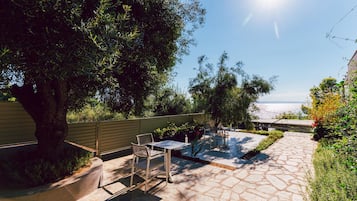 Un patio exterior con suelo de piedra, una mesa, sillas y vista al mar.