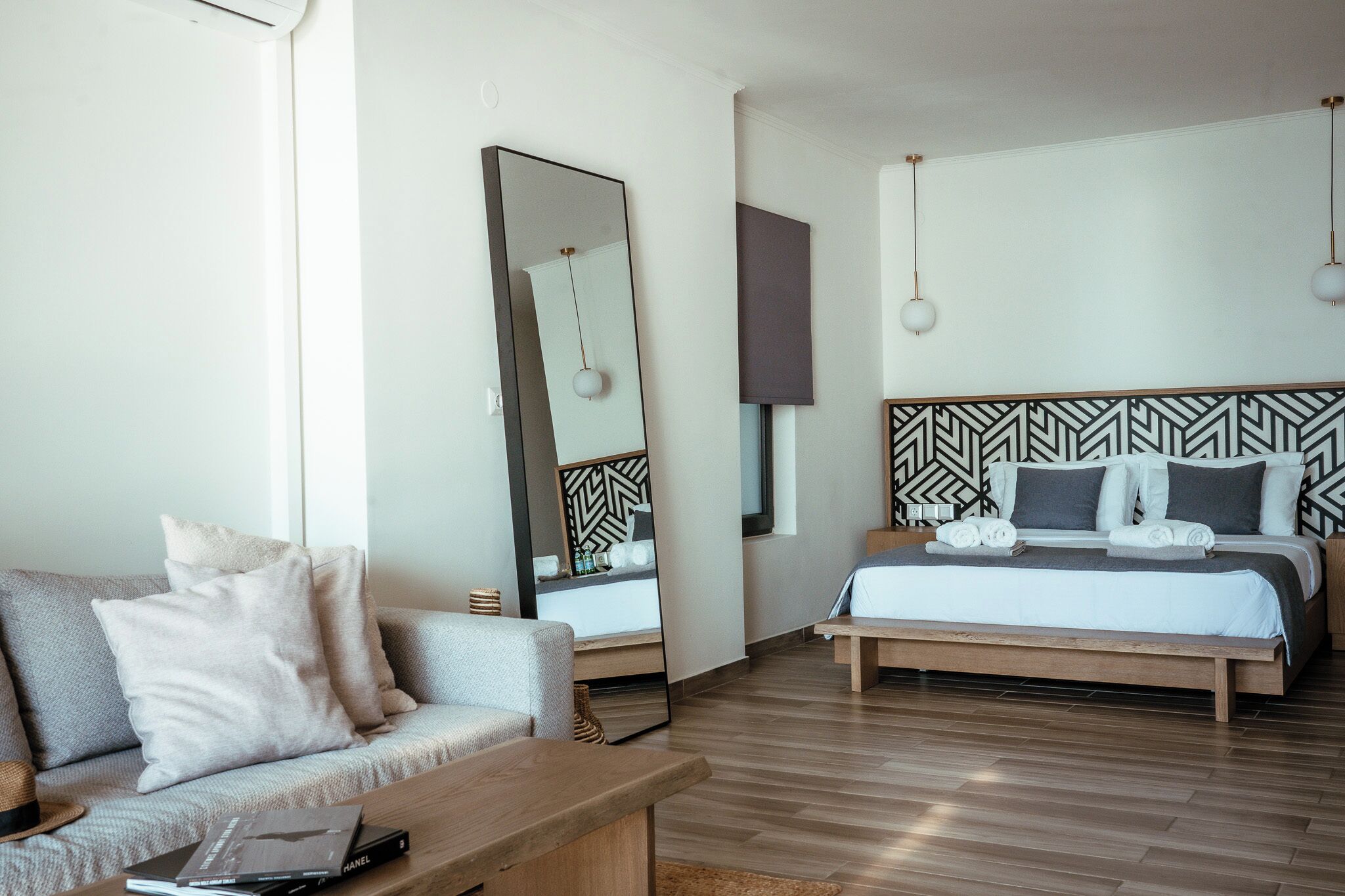 Habitación de hotel moderna con cama, sofá, mesa de centro, espejo grande y pared con diseño.