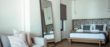 Habitación de hotel moderna con cama, sofá, mesa de centro, espejo grande y pared con diseño.