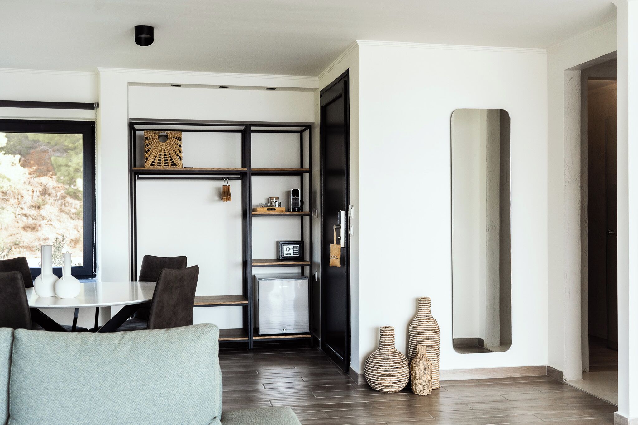 A modern living room with a dining area, featuring a sofa, a dining table with chairs, a built-in bookshelf, and a large mirror.