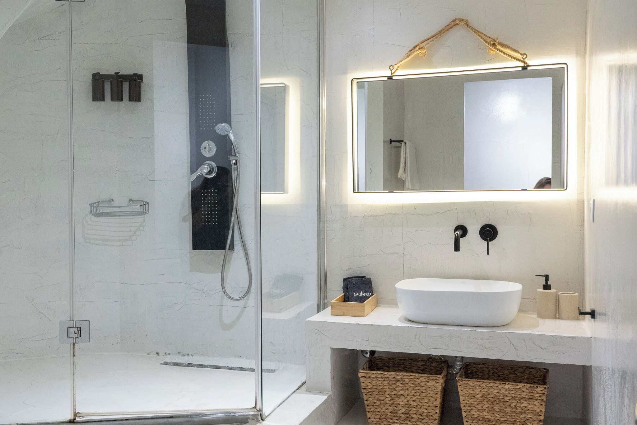 A modern bathroom with a glass-enclosed shower, a white sink, and a mirror with a light above it.