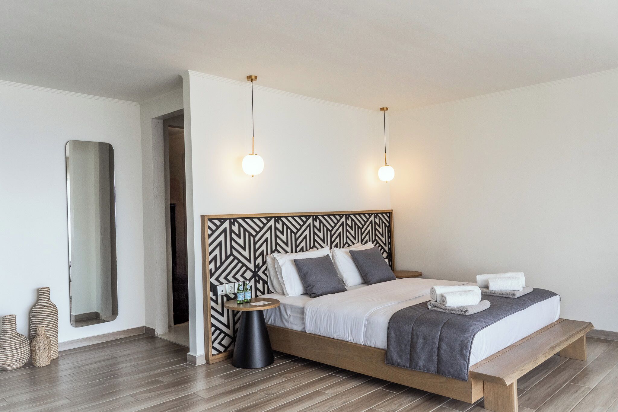 A modern bedroom with a wooden bed, a black and white patterned headboard, bedside tables, and a large mirror.