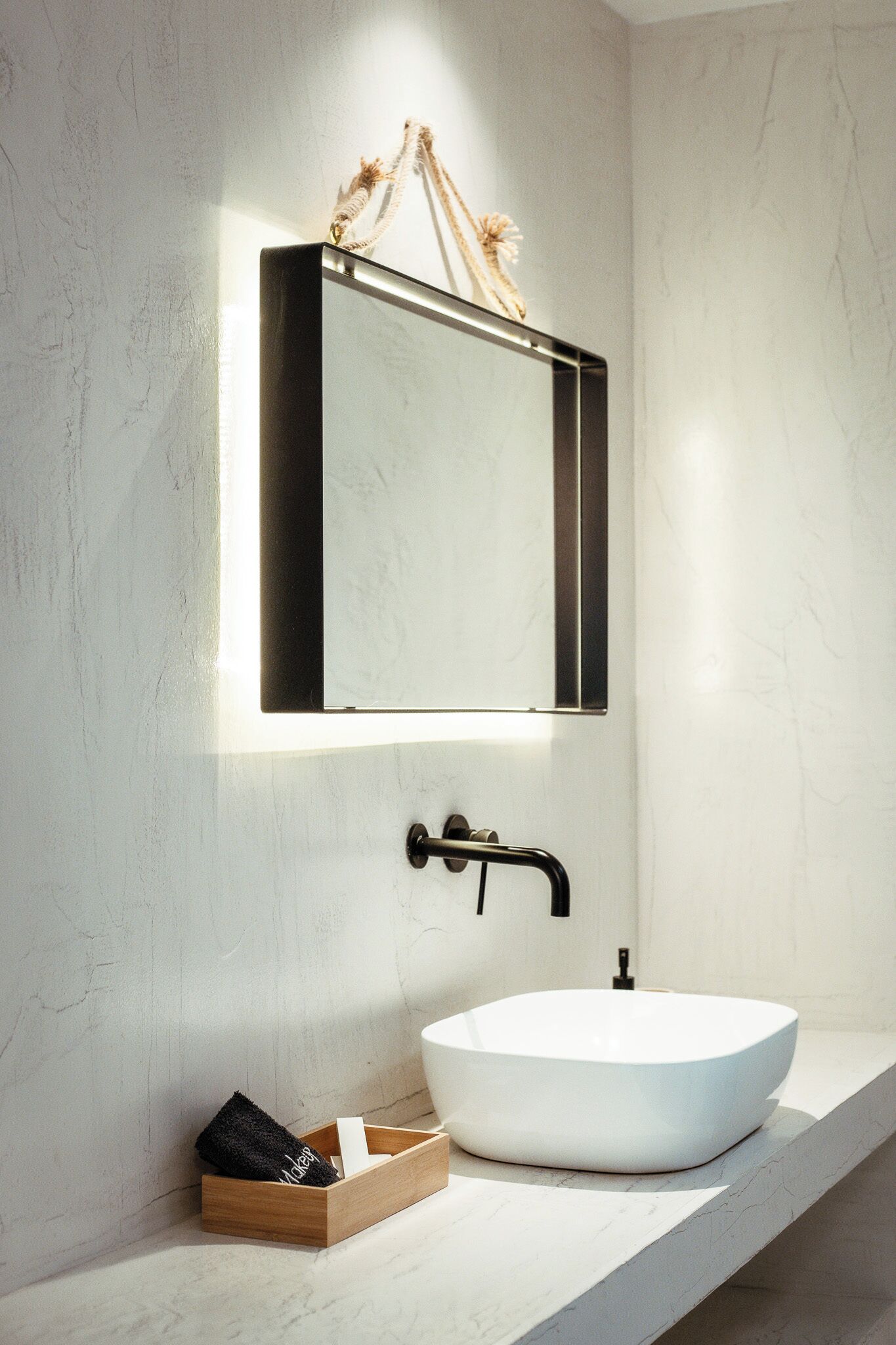 A modern bathroom with a white sink, a black faucet, and a rectangular mirror with a light above it.
