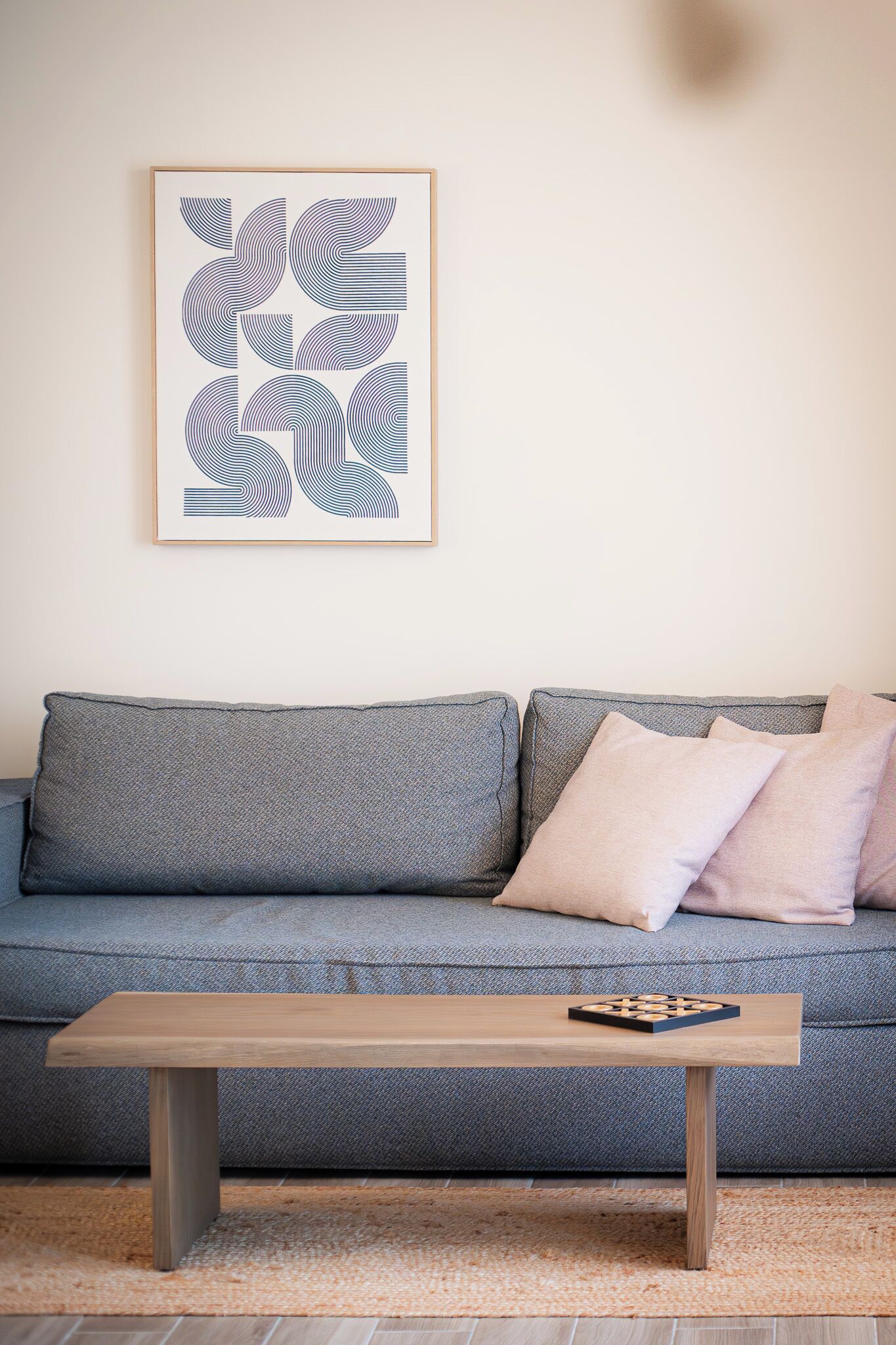 A modern living room with a grey sofa, a wooden coffee table, and a framed abstract artwork on the wall.