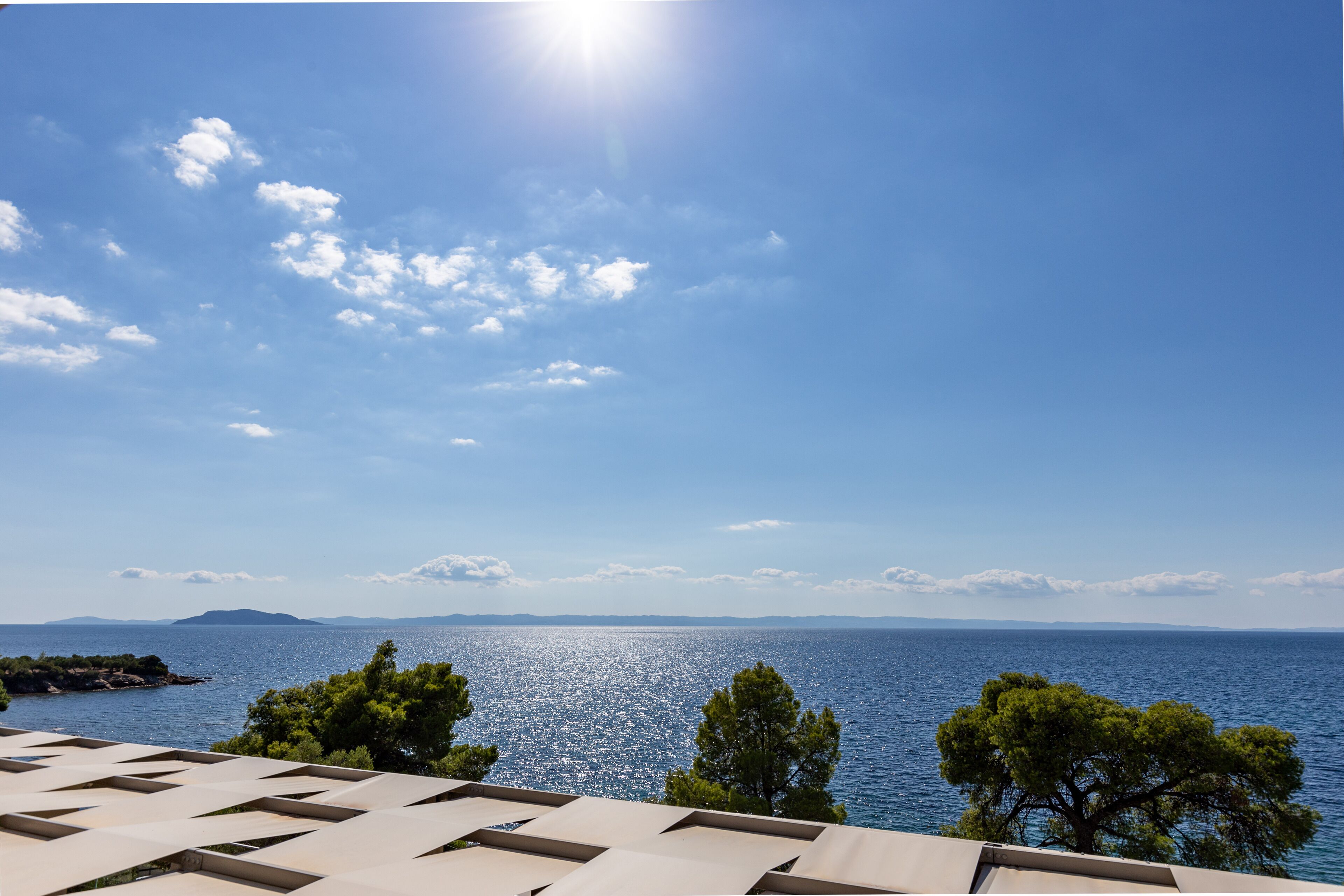 Eine Küstenansicht mit blauem Himmel, ruhiger See und einer fernen Landmasse.