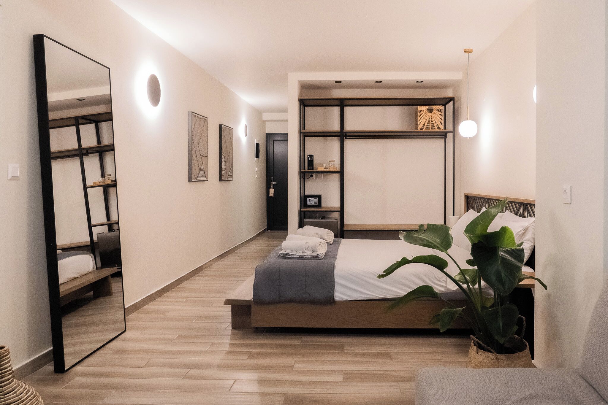 A modern bedroom with a bed, bedside tables, a mirror, and a potted plant.