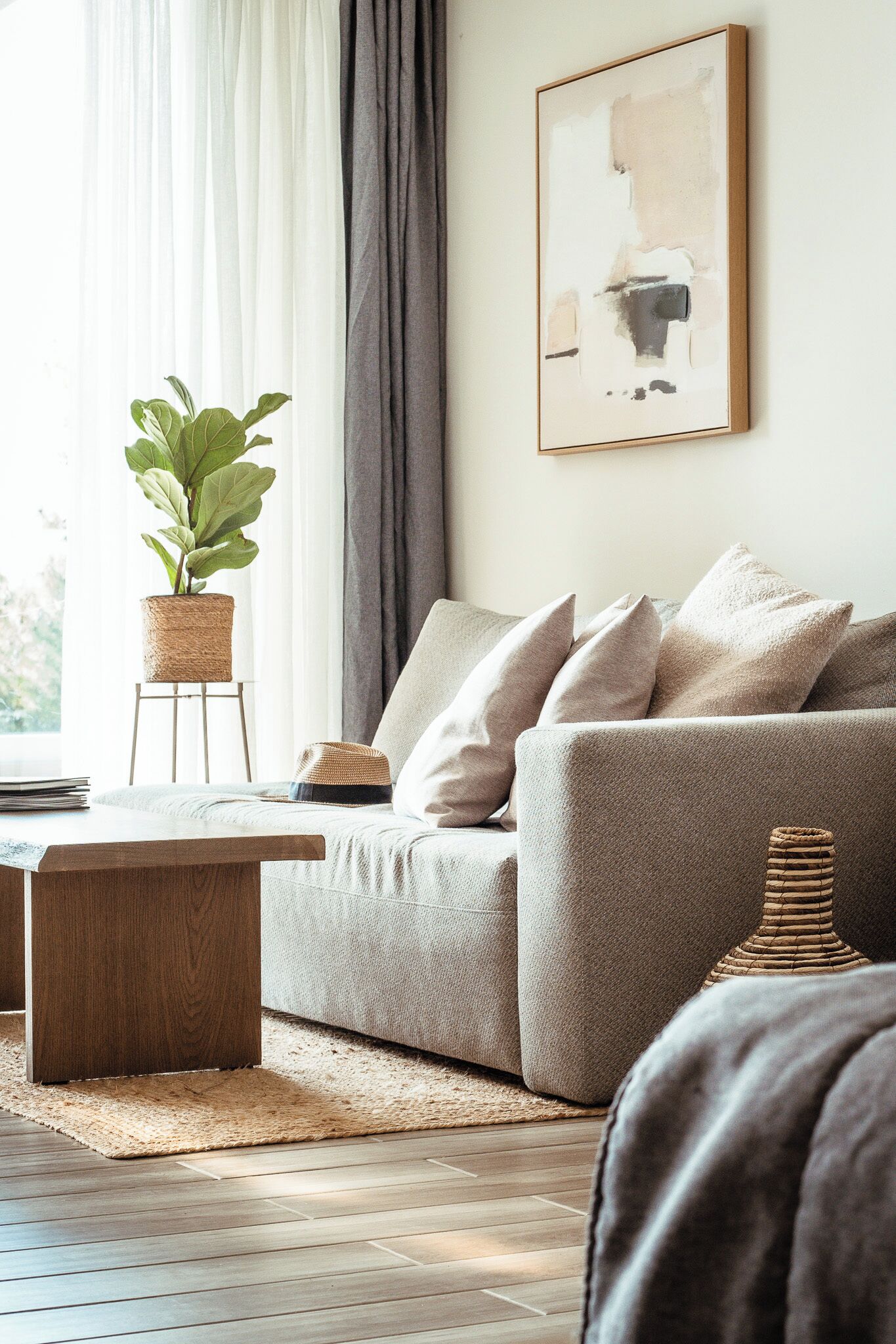 A living room with a sofa, a coffee table, a potted plant, and a framed abstract painting on the wall.