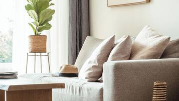 A living room with a sofa, a coffee table, a potted plant, and a framed abstract painting on the wall.