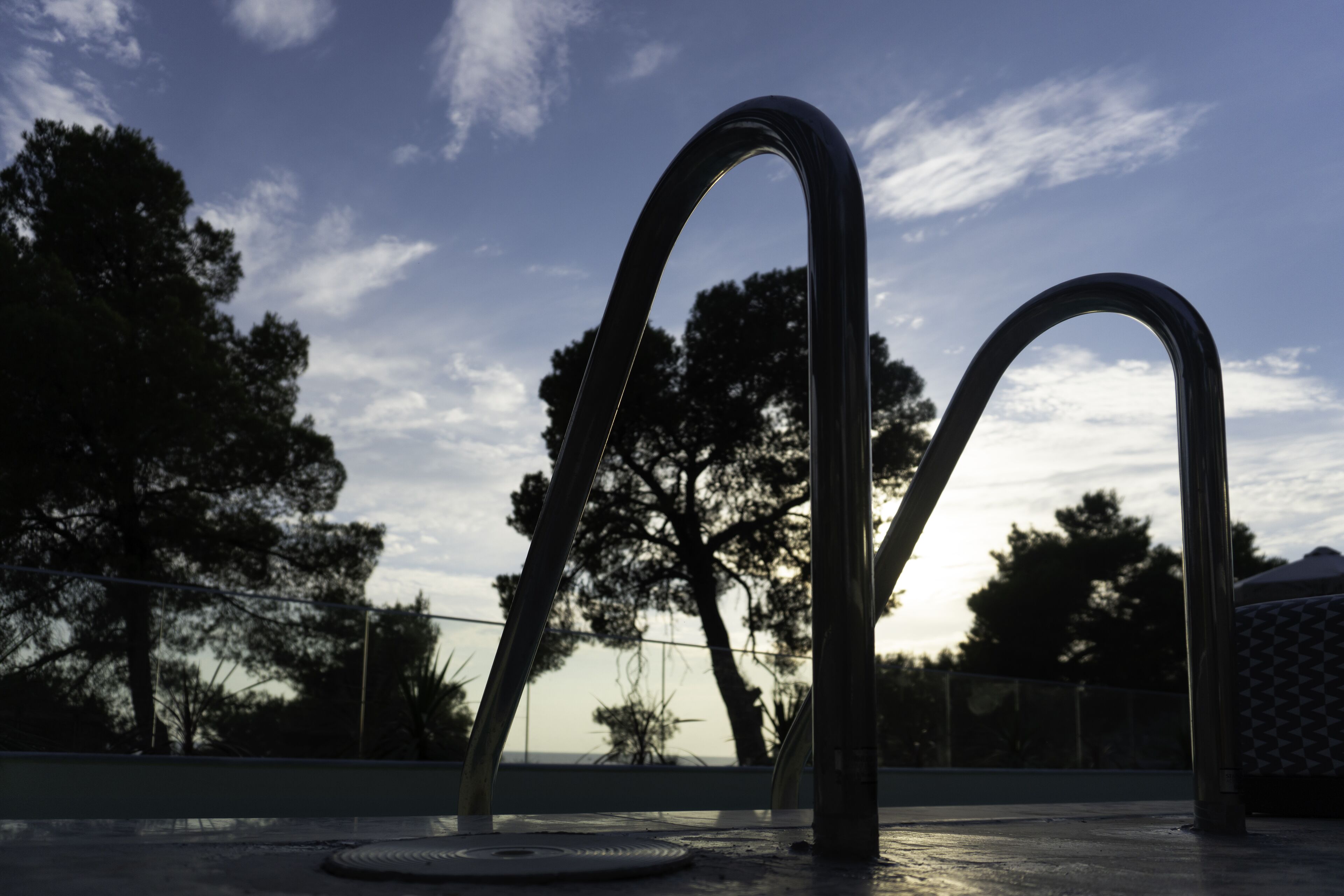 A metal structure with curved elements, possibly a sculpture, set against a backdrop of trees and a clear sky.