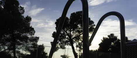 A metal structure with curved elements, possibly a sculpture, set against a backdrop of trees and a clear sky.