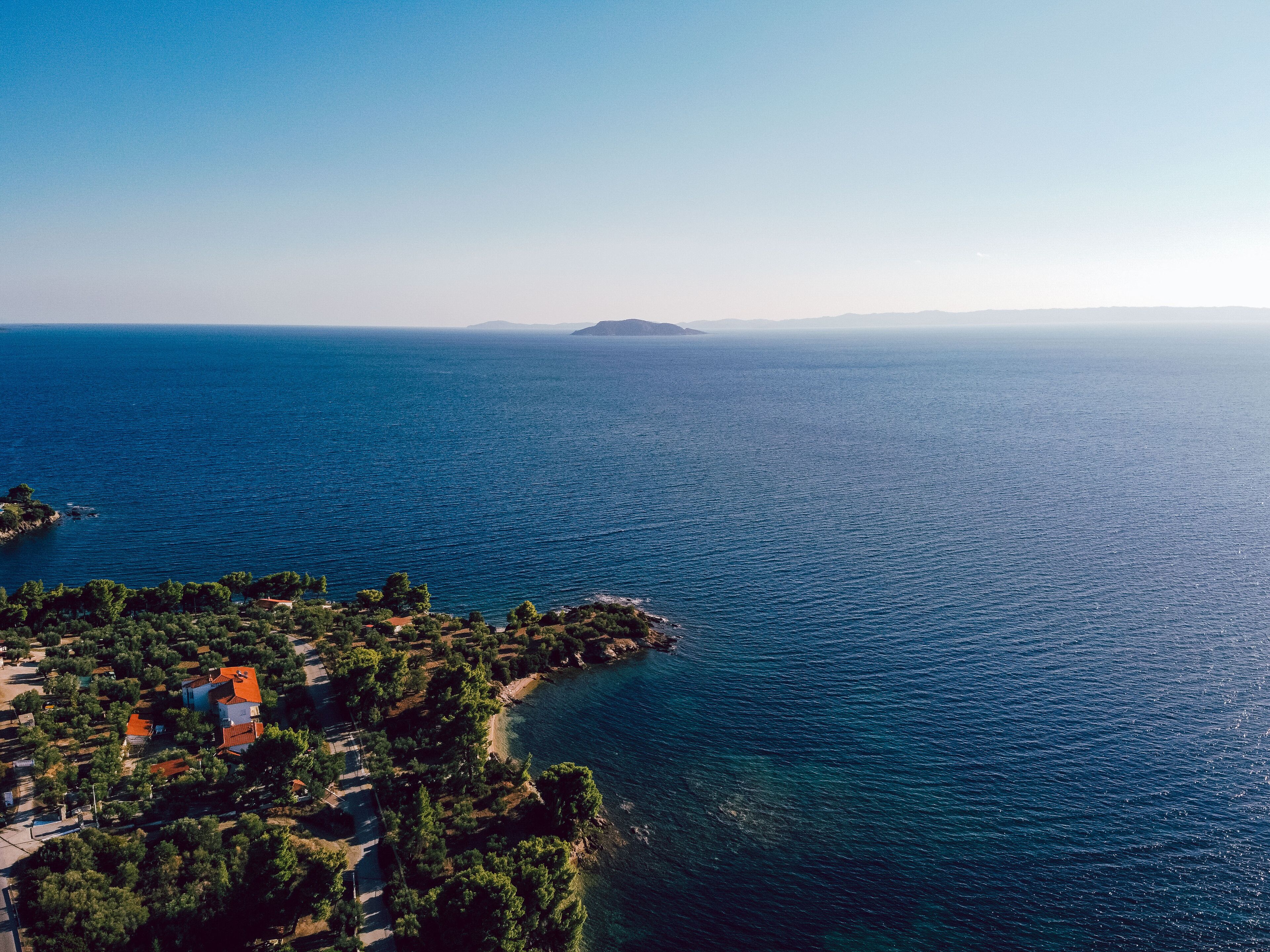 An aerial view of a coastal area with a small settlement, including houses and greenery, along the shoreline.