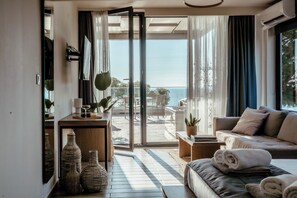A modern living room with a sofa, a coffee table, and a view of the sea through large glass doors. - Casa Bloo Adults Only by Still Collection (Sithonia)
