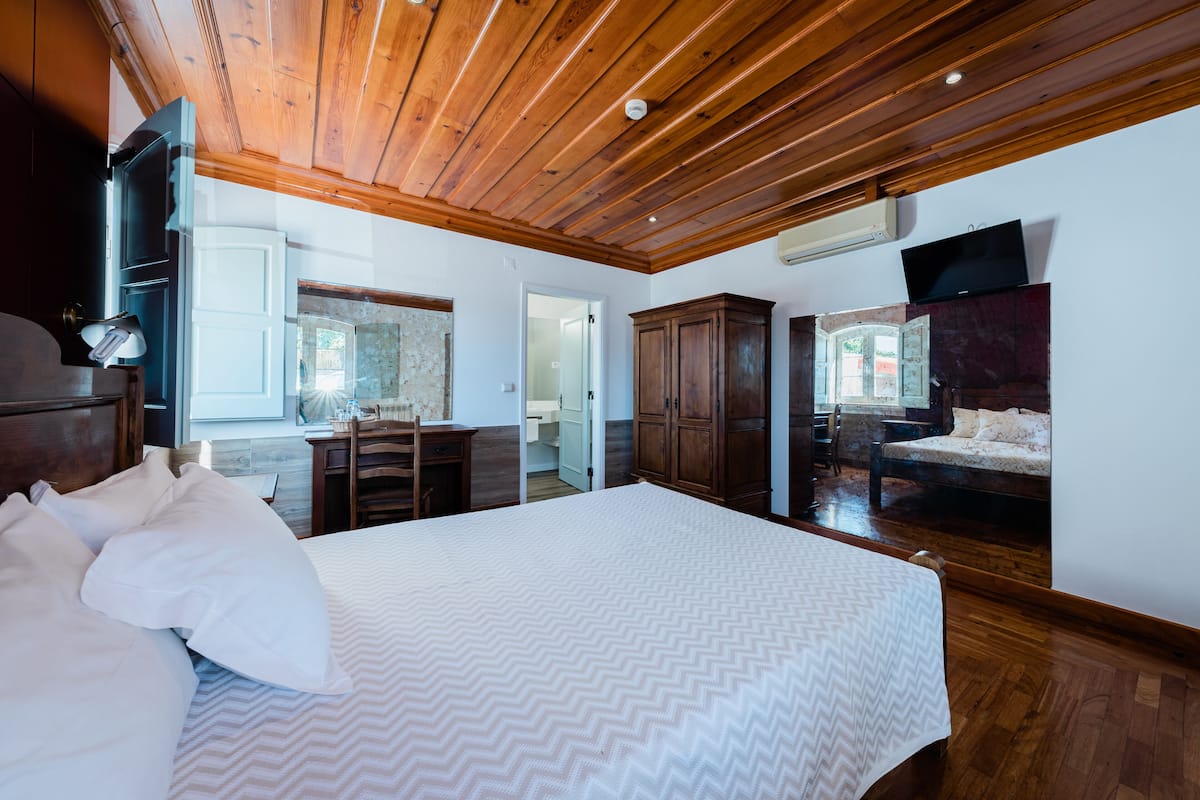Une chambre avec un grand lit, un plafond en bois et un téléviseur fixé au mur.