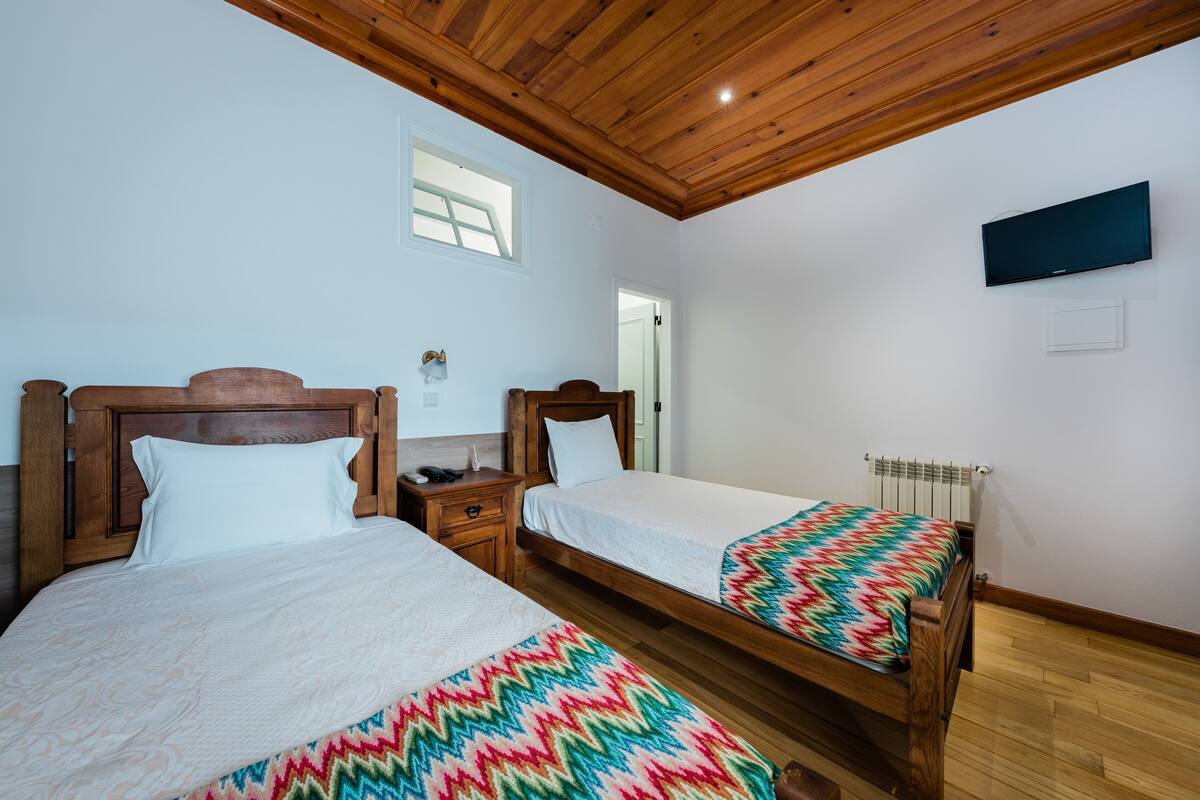 Une chambre avec deux lits en bois, un téléviseur fixé au mur et une fenêtre.
