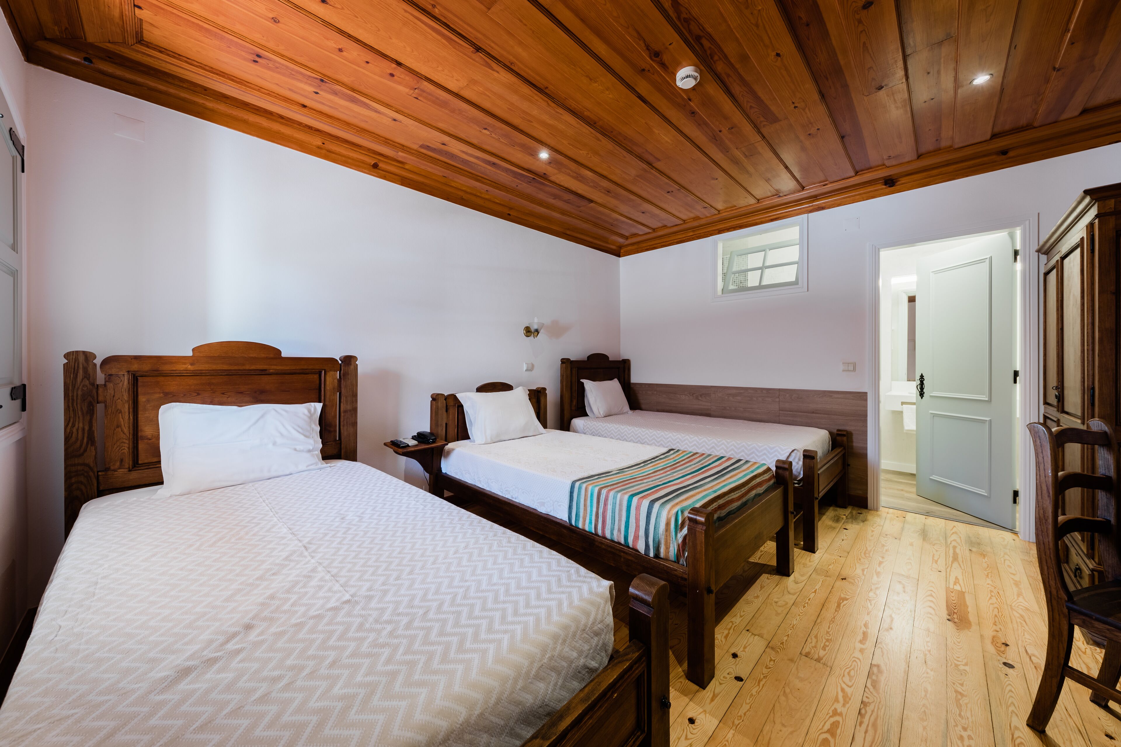 A room with three wooden beds, a wooden ceiling, and a door leading to another room.