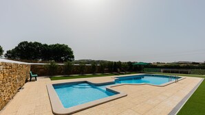 Una piscina de forma singular, rodeada por un muro de piedra y un césped cuidado.