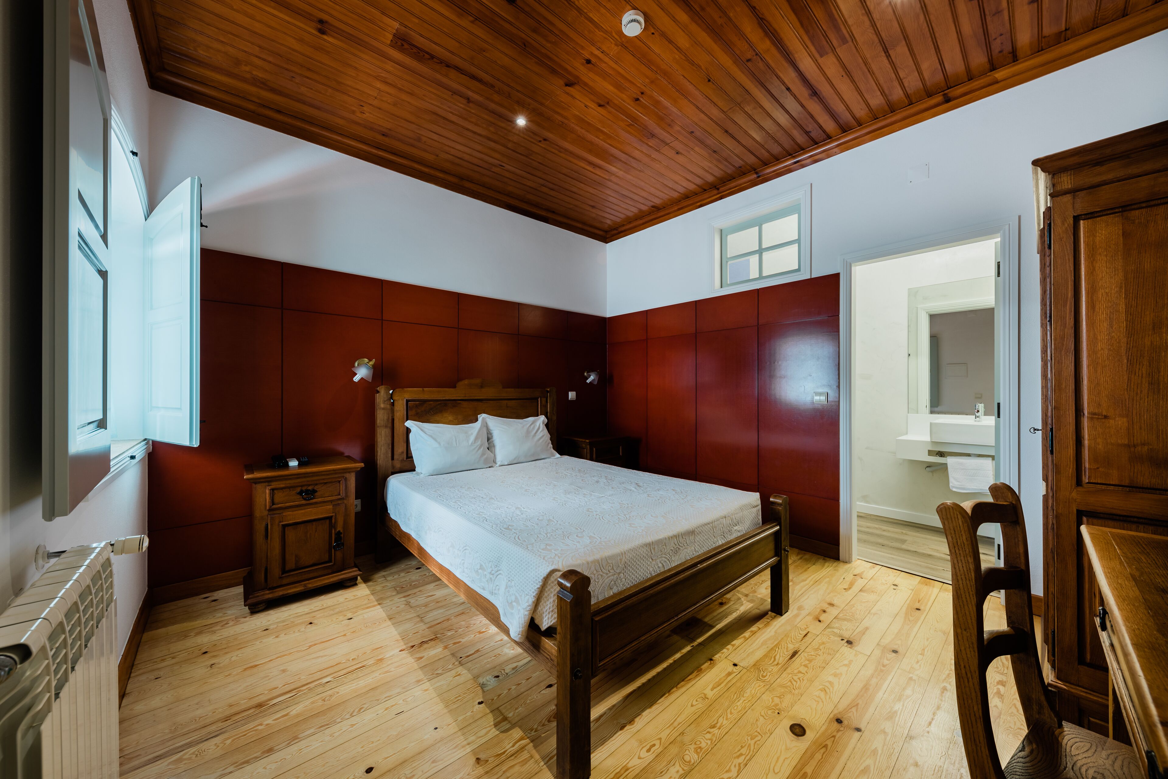 A bedroom with a wooden bed, a nightstand, a wooden chair, and a wooden ceiling.