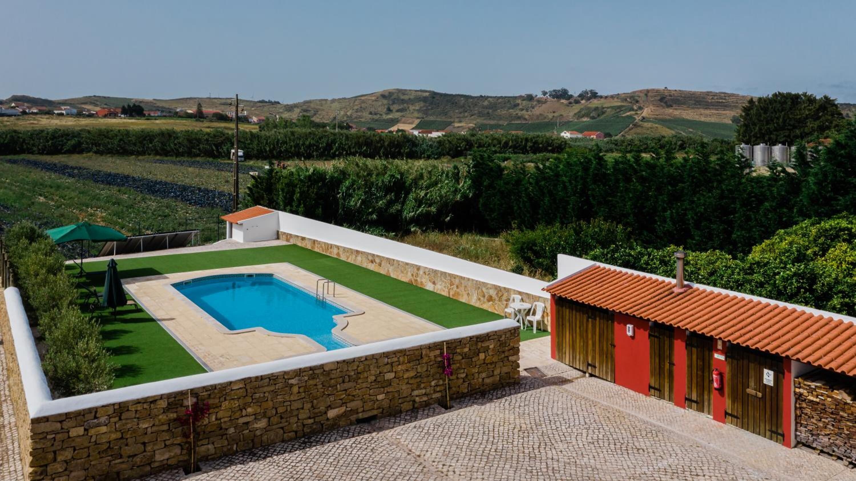 Une piscine avec un mur en pierre et un bâtiment rouge en arrière-plan.
