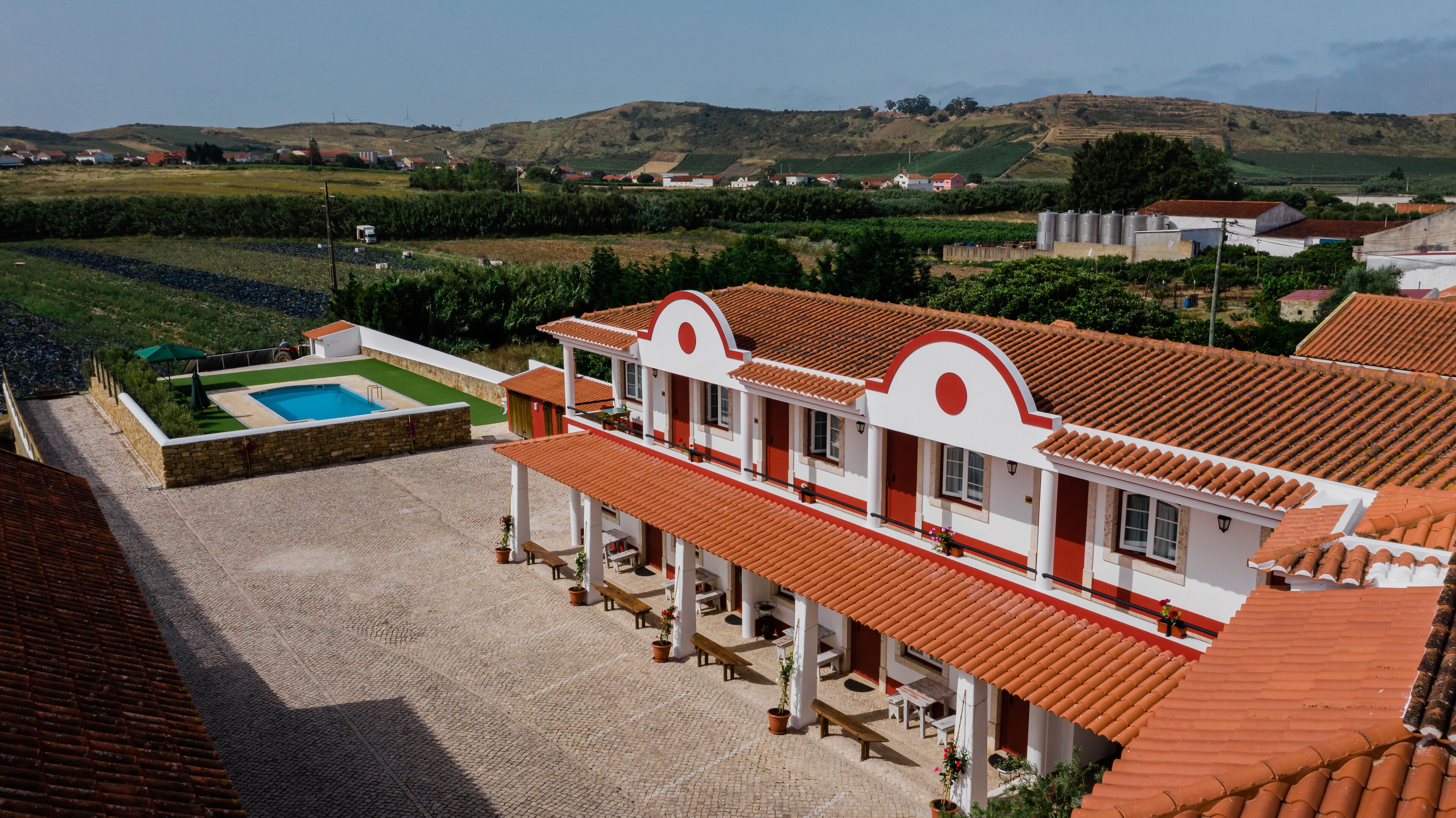 A large building with a red-tiled roof, a swimming pool, and a courtyard with potted plants.