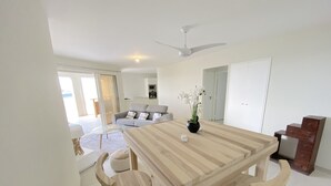 Ett modernt vardagsrum med ett stort matbord i trä, två trästolar, en grå soffa och en takfläkt.